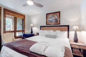 Habitación de hotel con cama, dos lámparas de noche, cabecera de madera, un cuadro en la pared y una ventana con persianas.