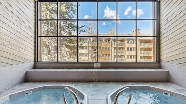 Ett spaområde med två bubbelpooler och ett stort fönster med utsikt över bostadshus.