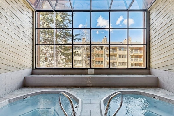 A spa area with two hot tubs and a large window offering a view of residential buildings. - Spacious, in-town condo with balcony, pools, hot tub, tennis - walk to lifts (Breckenridge)