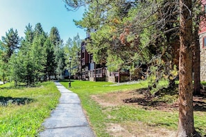 A pathway leading to a building with a stone facade and a wooden deck. - Spacious, in-town condo with balcony, pools, hot tub, tennis - walk to lifts (Breckenridge)