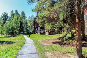 A pathway leading to a building with a stone facade and a red roof, surrounded by trees and grass. - Ideally located condo with pool, hot tubs & sauna - walk to lifts & Main Street (Breckenridge)