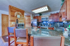 A kitchen with wooden cabinets, a microwave, a refrigerator, and a dining area with chairs. - Ideally located condo with pool, hot tubs & sauna - walk to lifts & Main Street (Breckenridge)