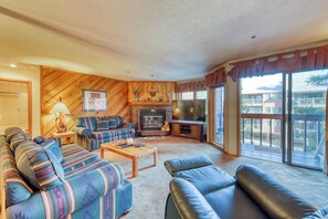 A cozy living room with a fireplace, a sofa set, a coffee table, and a large window with a view. - Ideally located condo with pool, hot tubs & sauna - walk to lifts & Main Street (Breckenridge)