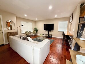 Ein Wohnzimmer mit einem Ecksofa, einem Fernseher, einem Esstisch und einer Küchenzeile.