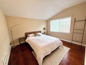 Ein Schlafzimmer mit Bett, einem Fenster mit Jalousien, einem Heizkörper und einer Stehlampe.