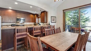 A kitchen with wooden cabinets, a microwave, and a dining area with a table and chairs. - Main Street condo with mountain view, fireplace, pool & hot tubs - walk to lifts (Breckenridge)