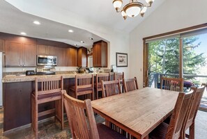 A kitchen with wooden cabinets, a microwave, and a dining area with a table and chairs. - Main Street condo with mountain view, fireplace, pool & hot tubs - walk to lifts (Breckenridge)