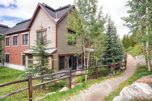 A modern two-story house with a covered patio, surrounded by a wooden fence and a gravel path. - Main Street condo with mountain view, fireplace, pool & hot tubs - walk to lifts (Breckenridge)