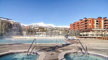A pool area with hot tubs, a mountain in the background, and a red building with balconies.
