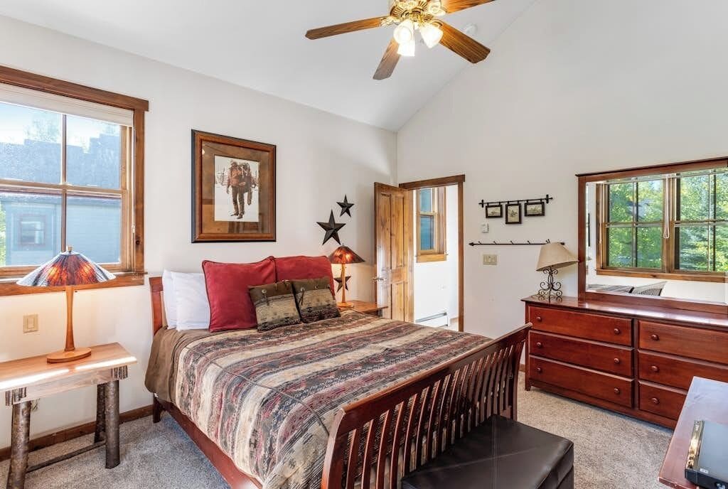 A bedroom with a bed, a desk, a dresser, and a ceiling fan.