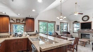 A spacious kitchen with granite countertops, wooden cabinets, and a large island. There is a dining area with wooden chairs and a fireplace. - Main Street condo with mountain view, fireplace, pool & hot tubs - walk to lifts (Breckenridge)
