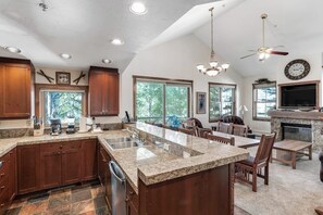 A spacious kitchen with granite countertops, wooden cabinets, and a large island. There is a dining area with wooden chairs and a fireplace. - Main Street condo with mountain view, fireplace, pool & hot tubs - walk to lifts (Breckenridge)