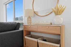 A modern living room with a grey sofa, a wooden console table with a lamp, a mirror, and a vase with dried plants. - The Spoonbill Retreat | Water Views Family Escape (Sorell)