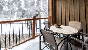 Ein hölzerner Balkon mit Tisch und Stühlen, mit Blick auf eine verschneite Landschaft aus Bäumen und Gebäuden.
