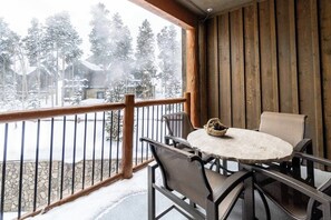 Ein hölzerner Balkon mit Tisch und Stühlen, mit Blick auf eine verschneite Landschaft aus Bäumen und Gebäuden.