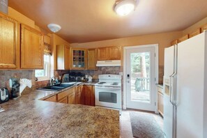 A kitchen with wooden cabinets, a granite countertop, a white stove, and a refrigerator. - 3-Story Hideaway with Game Room & Direct Forest Access — Dogs Welcome! (Breckenridge)
