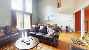 Ein geräumiges Wohnzimmer mit einem dunkelgrünen Ledersofa, einem runden Couchtisch und einem Deckenventilator.