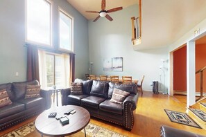 A spacious living room with a dark leather sofa, a round coffee table, and a ceiling fan. - 3-Story Hideaway with Game Room & Direct Forest Access — Dogs Welcome! (Breckenridge)