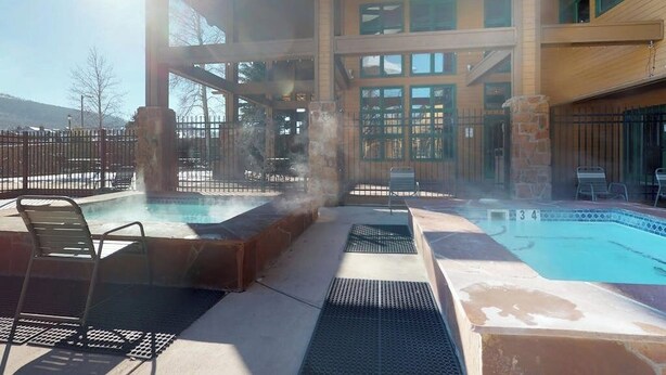 A pool area with a hot tub, lounge chairs, and a building with multiple windows. - 3rd-floor retreat with balconies, in/outdoor pools, game room, gym, views (Granby)