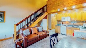 A cozy living area with a brown leather sofa, a wooden staircase, and a kitchen with wooden cabinets and a microwave. - 3rd-floor retreat with balconies, in/outdoor pools, game room, gym, views (Granby)