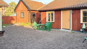 En træbygning med en grusgård, en trædør og et vindue med hvid ramme.