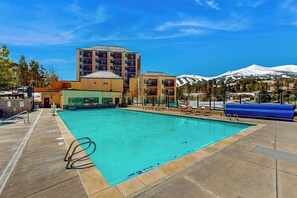 Ein Swimmingpool mit Liegestühlen, ein mehrstöckiges Gebäude und ein Berg im Hintergrund.