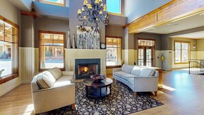 A spacious living room with a fireplace, two sofas, a chandelier, and large windows. - Top-floor downtown condo with pool, hot tubs & gym, walk to ski lifts (Breckenridge)