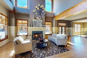 Ein geräumiges Wohnzimmer mit Kamin, zwei Sofas, einer Kristallleuchtre und großen Fenstern.