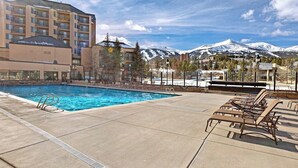 A hotel pool with lounge chairs, a clear sky, and snow-capped mountains in the background. - Mountain condo with pool, hot tubs, gym & steam room - near skiing & hiking (Breckenridge)