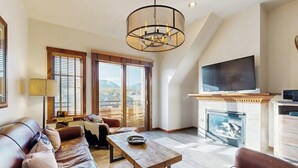 A living room with a sofa, a coffee table, a fireplace, a TV, and a view of the outdoors. - Mountain condo with pool, hot tubs, gym & steam room - near skiing & hiking (Breckenridge)