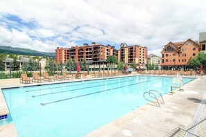 A swimming pool with lounge chairs and umbrellas, surrounded by multi-story buildings with balconies. - Luxury ski condo steps from QuickSilver Lift with pool, hot tubs & gym (Breckenridge)