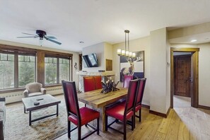 A dining area with a wooden table, red upholstered chairs, a ceiling fan, a mounted TV, and a fireplace with a deer head decoration. - Luxury ski condo steps from QuickSilver Lift with pool, hot tubs & gym (Breckenridge)