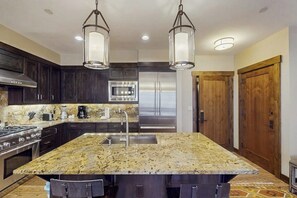 Una cocina moderna con alacenas de madera oscura, electrodomésticos de acero inoxidable, una isla de granito e iluminación colgante.