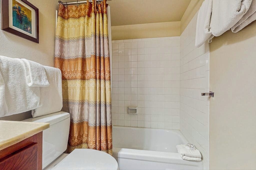 A bathroom with a shower curtain, a toilet, a bathtub, and a towel rack.