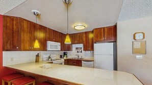 Eine Küche mit Holzausstattung, einer weißen Arbeitsplatte, einer Mikrowelle, einem Kühlschrank und einer Uhr an der Wand.