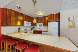 Eine Küche mit Holzausstattung, einer weißen Arbeitsplatte, einer Mikrowelle, einem Kühlschrank und einer Uhr an der Wand.