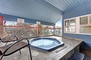 A hot tub with a view of trees and mountains, a covered patio with chairs, and a sign indicating a maximum number of persons allowed. - Beautiful downtown condo with WiFi, pool, hot tub, gym, & balcony - near lifts (Breckenridge)