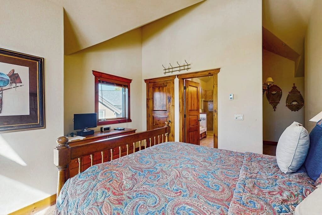 Een slaapkamer met een bed, een bureau met een computer, een raam en een deur naar een andere kamer.