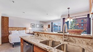 A hotel room with a bed, a marble kitchen island with a sink, a wooden headboard, and a large window with a view. - Skiers studio with WiFi, pool, hot tub, sauna, & balcony in downtown location (Breckenridge)
