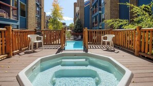 A hot tub on a wooden deck with a pool in the background, surrounded by buildings. - Skiers studio with WiFi, pool, hot tub, sauna, & balcony in downtown location (Breckenridge)