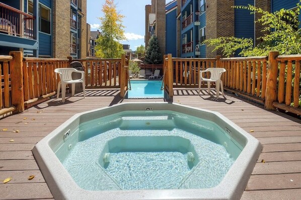A hot tub on a wooden deck with a pool in the background, surrounded by buildings. - Skiers studio with WiFi, pool, hot tub, sauna, & balcony in downtown location (Breckenridge)