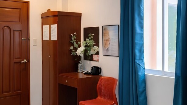 Quarto com escrivaninha de madeira, cadeira vermelha, armário, vaso com flores e janela com cortinas.