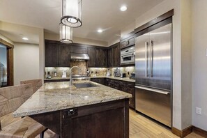 A modern kitchen with dark wood cabinets, stainless steel appliances, and a granite countertop. - Modern mountain condo with balcony, pool & hot tubs, walk to lifts/downtown (Breckenridge)