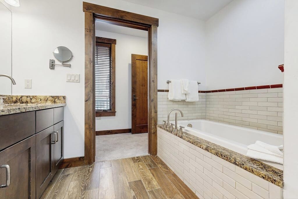 Un baño con puerta de madera, bañera blanca, encimera de granito y un espejo.