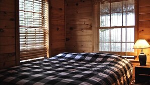 Una camera in legno con un letto, una finestra con tende e un comodino con una lampada.