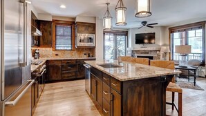 Una cocina moderna con una isla grande, armarios de madera, electrodomésticos de acero inoxidable e iluminación colgante.