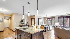 Una cocina moderna con una isla central, iluminación colgante y un comedor con sofá y sillas.
