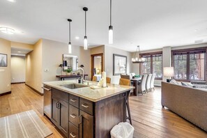 A modern kitchen with a central island, pendant lighting, and a dining area with a sofa and chairs. - Downtown condo with pool, hot tubs & gym - walk to lifts, near everything (Breckenridge)