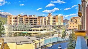 Un hotel de varios pisos con balcones, piscina y vistas a un lago y montañas.