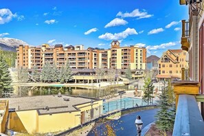 A multi-story hotel with balconies, a swimming pool, and a view of a lake and mountains. - Downtown condo with pool, hot tubs & gym - walk to lifts, near everything (Breckenridge)
